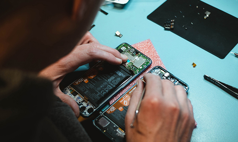 Technician using precision tools to repair an opened mobile phone
